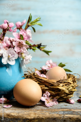 Easter background with easter eggs in nest , blooming flowers on old wooden table with copy space