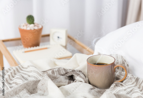 Cup of coffee on cozy white bed with cactus flowerpot,memo pat and alarm clock on wood bed side table