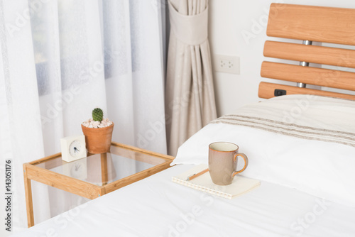 Cup of coffee on cozy white bed with cactus flowerpot,memo pat and alarm clock on wood bed side table © jcsmilly