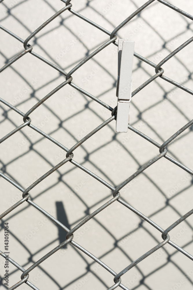 Fototapeta premium White wooden cloth pin over metal wire fence with shadow on cement wall backgroun