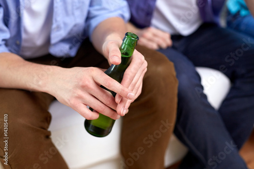 men with beer bottles sitting on sofa at home