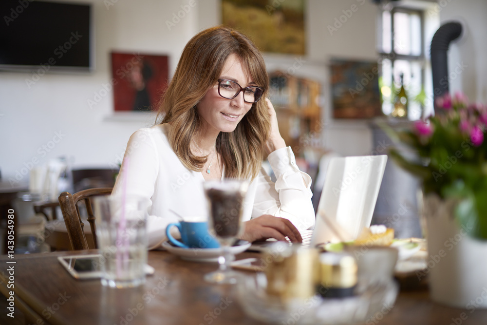 Working online. Shot of a middle aged woman sitting in cafe and working on laptop. Working online. Shot of a middle aged woman sitting in cafe and working on laptop.