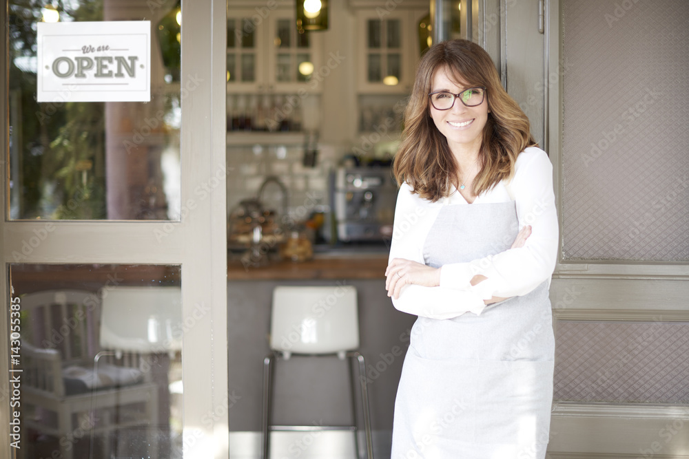 Proud small coffee shop owner businesswoman. Shot of a happy barista woman standing at doorway and inviting to her coffee shop. Small business. Proud small coffee shop owner businesswoman. Shot of a happy barista woman standing at doorway and inviting to her coffee shop. Small business.