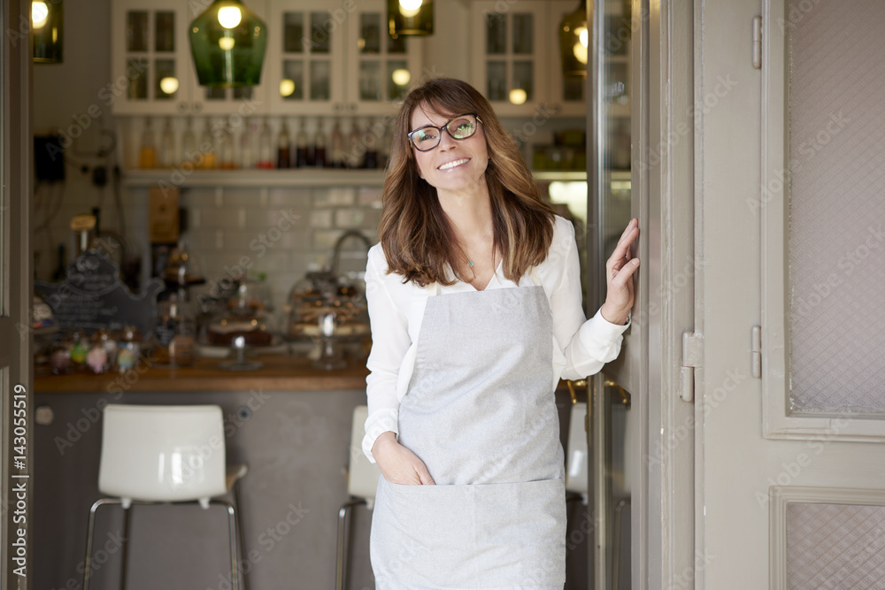 Proud small coffee shop owner businesswoman. Shot of a happy barista woman standing at doorway and inviting to her coffee shop. Small business. Proud small coffee shop owner businesswoman. Shot of a happy barista woman standing at doorway and inviting to her coffee shop. Small business.