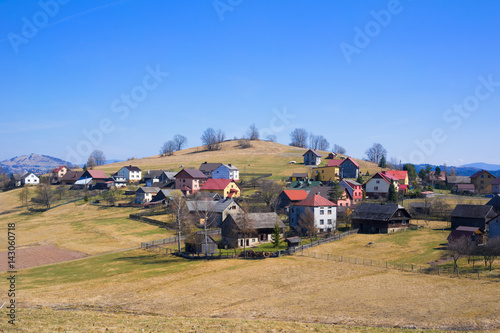 Traditional rural landscape and small village in the central Europe - houses, farms, fields, hills and meadows. Yellow grass and bare tree during spring season