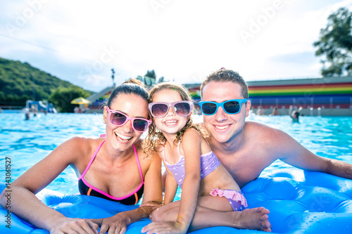 Mother, father and daughter in swimming pool. Sunny summer. © Halfpoint