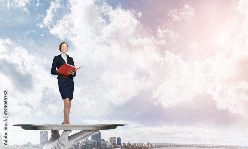 Attractive businesswoman on metal tray with red book in hands against cityscape background Attractive businesswoman on metal tray with red book in hands against cityscape background
