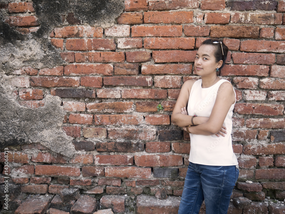 The woman stands looking at the wall with a dark brick background.