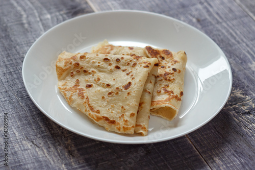 Homemade pancakes for a breakfast on a white plate on a wooden background