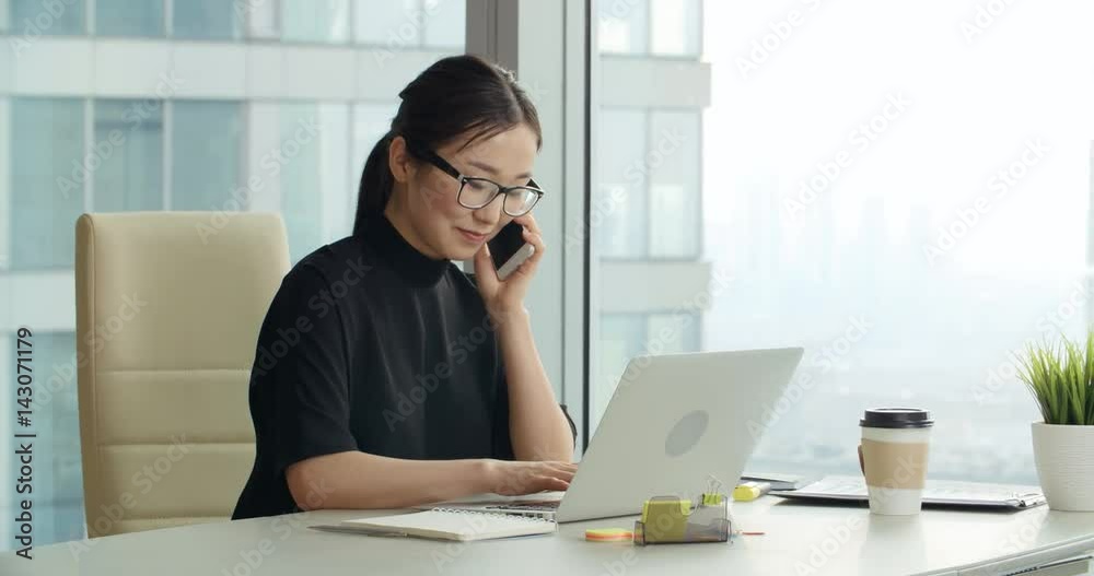 Asian girl with a smile talking on the phone in modern office Asian girl with a smile talking on the phone in modern office