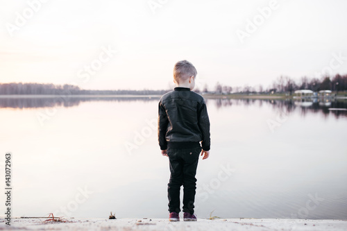 Little boy stands near the water at sunset. Conceptual photo 