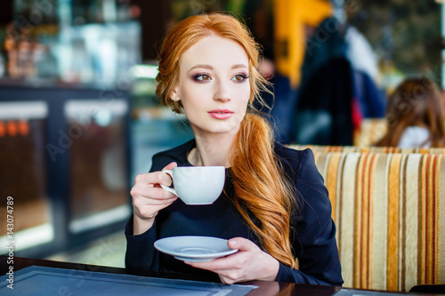 Pretty redhead young woman in the cafe with cup of tea