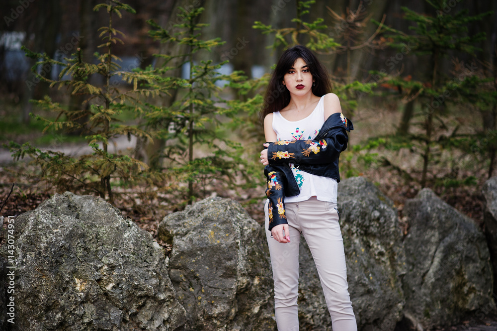 Brunette gypsy girl posed against stones on park. Model wear on leather jacket and t-shirt with ornament, pants. Brunette gypsy girl posed against stones on park. Model wear on leather jacket and t-shirt with ornament, pants.