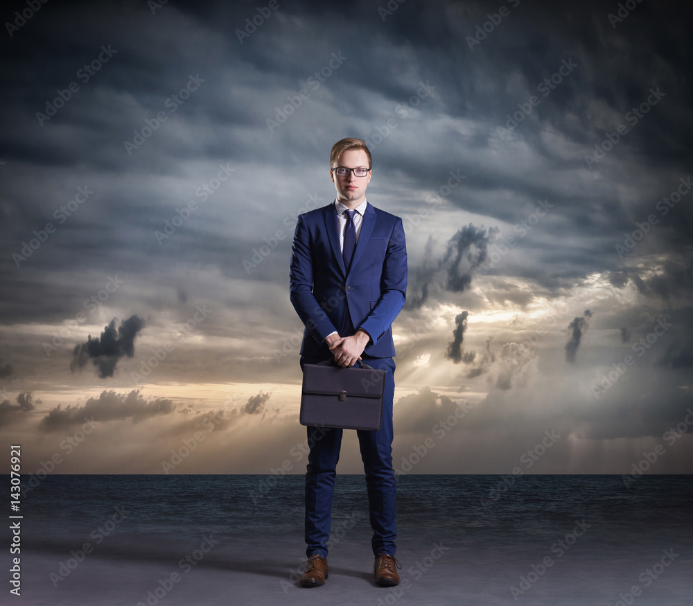 Businessman with briefcase standing on a dark, dramatic ocean background. Business concept. Businessman with briefcase standing on a dark, dramatic ocean background. Business concept.