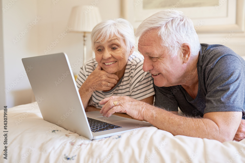 Happy senior couple using a laptop together in bed