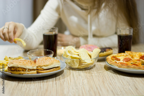 The girl is sitting at the table and eating fast food.