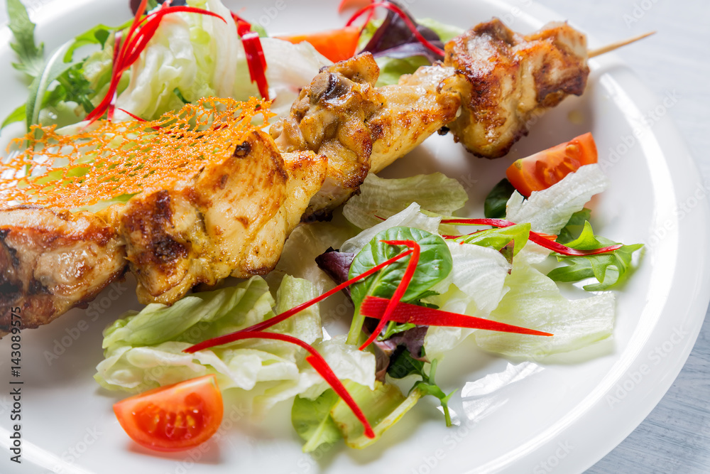 Chicken grilled meat on stick with salad and tomatoes on white plate. Close up with selective focus Chicken grilled meat on stick with salad and tomatoes on white plate. Close up with selective focus