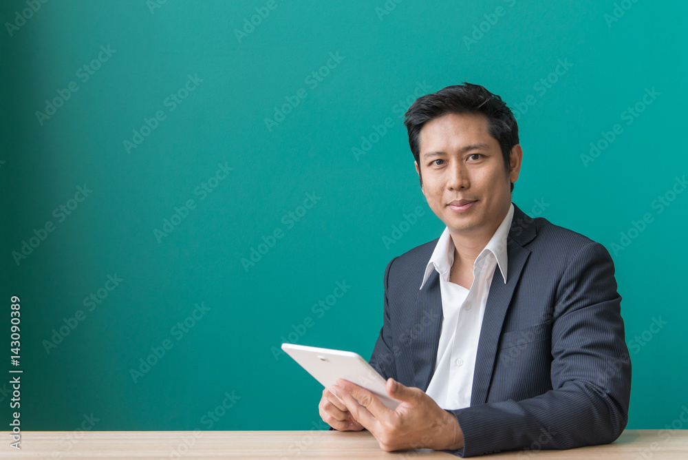 Portrait of businessman smiling and using pad at desktop against of blue wall. Vintage filtered image. Portrait of businessman smiling and using pad at desktop against of blue wall. Vintage filtered image.