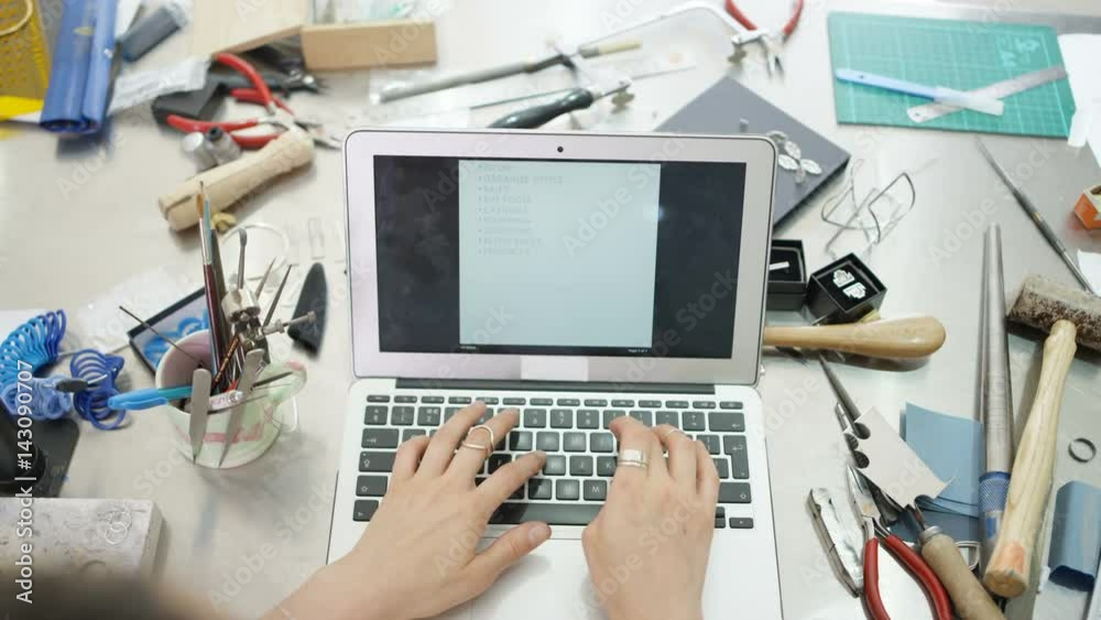  Jewelry designer at workbench making a to do list on computer. Close up on hands, no faces. 