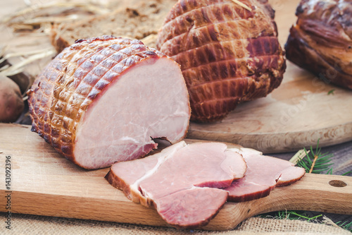 Ham on wooden desk. Rustic background with hay and meat slices.
