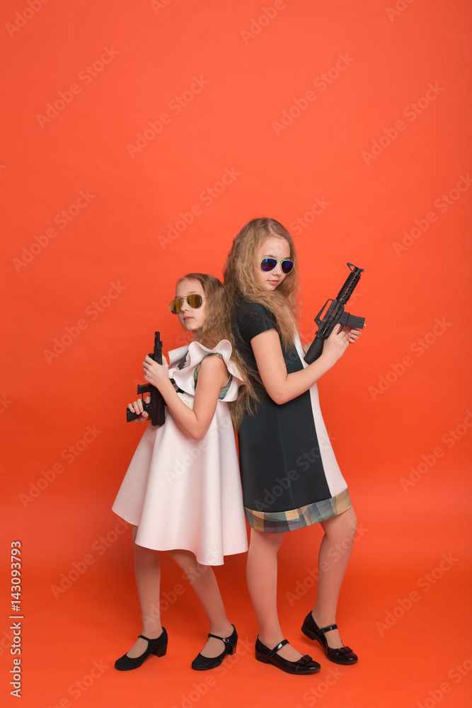 Two girls in military dresses with arms in hand and sunglasses on red background Two girls in military dresses with arms in hand and sunglasses on red background