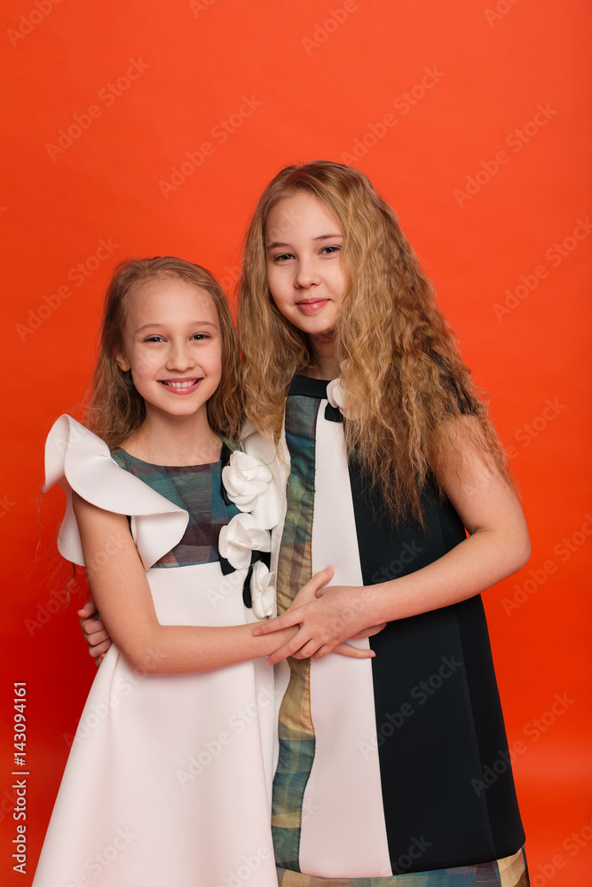 Two sisters in beautiful stylized dresses on a red background in the studio Two sisters in beautiful stylized dresses on a red background in the studio