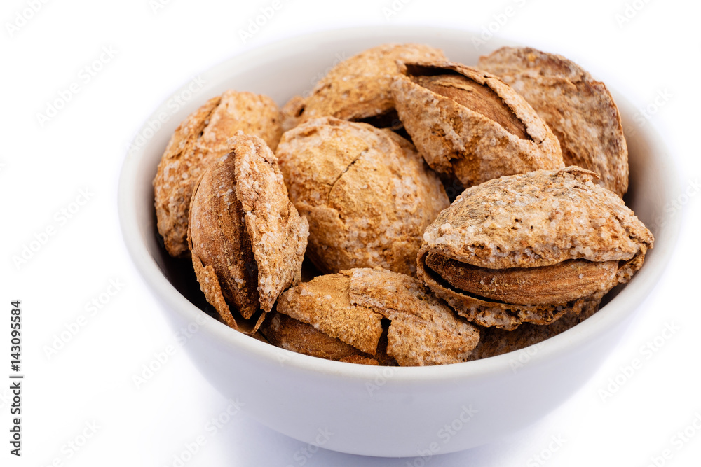 Fototapeta premium salted almonds in shell on white plate macro on white background
