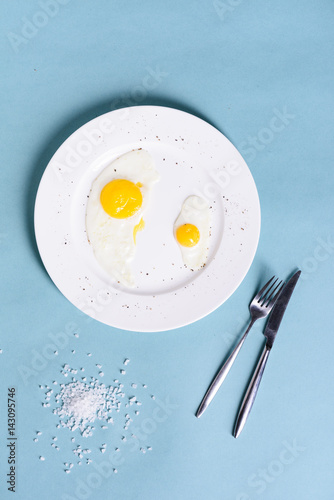 Healthy delicious breakfast of fried eggs with salt and pepper in a white plate on a blue table background. Top view, text space, flat lay.
