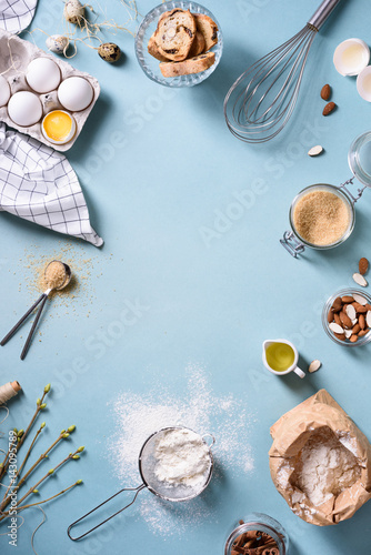 Bakery background frame. Fresh cooking ingredients - egg, flour, sugar, butter, nuts over blue background. Spring cooking theme. Top view, copy space.