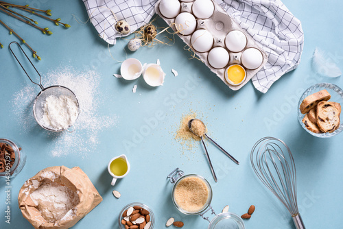 Bakery ingredients - flour, eggs, butter, sugar, yolk, almond nuts on blue table. Sweet pastry baking concept. Flat lay, copy space, top view.