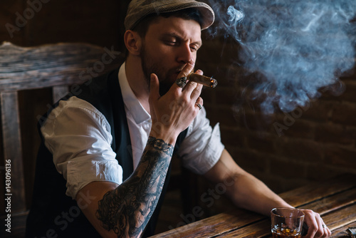 A young bearded man smoking a cigar in a pub