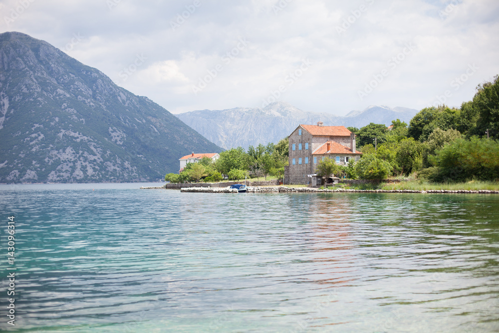 Stone house by blue sea and mountains. Cozy authentic house has beach, dock with boat, garden, blue bets and orange tiled roof at Boka Kotor bay in Montenegro. Stone house by blue sea and mountains. Cozy authentic house has beach, dock with boat, garden, blue bets and orange tiled roof at Boka Kotor bay in Montenegro.