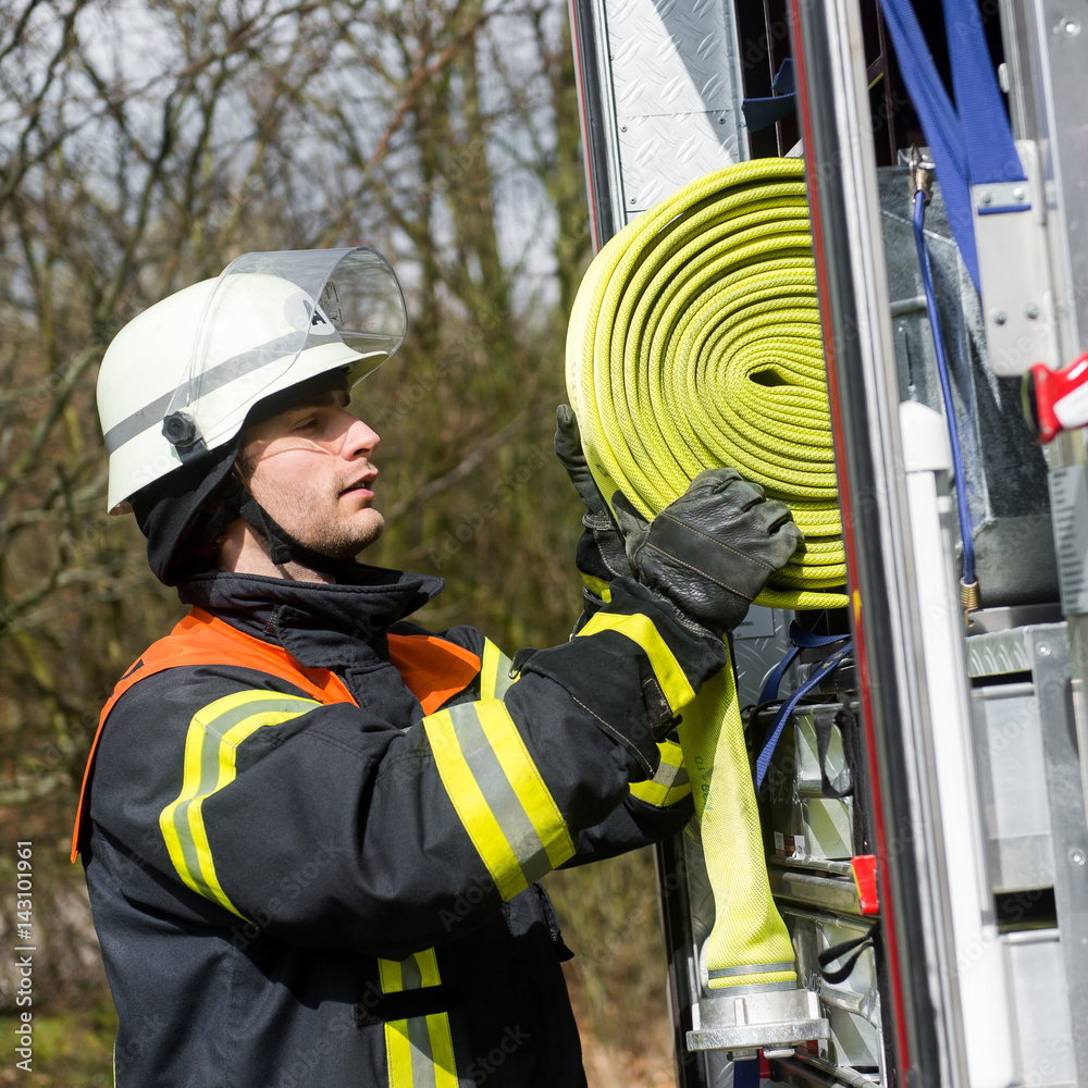 Obraz premium Feuerwehrmann holt einen Schlauch vom Löschfahrzeug