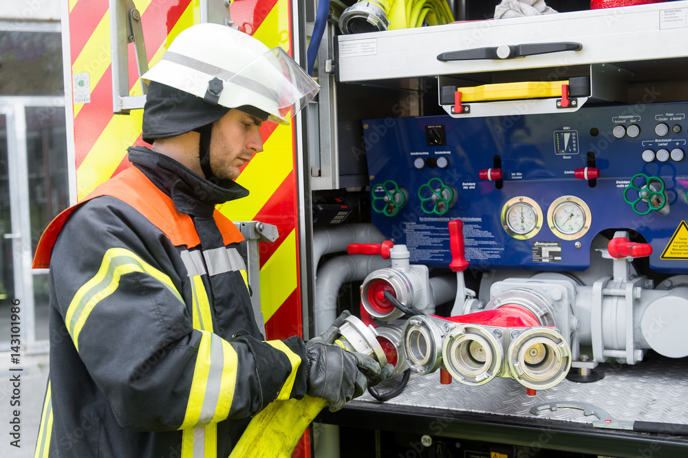 Fototapeta premium Mechanik straży pożarnej podłącza wąż do pompy wozu strażackiego