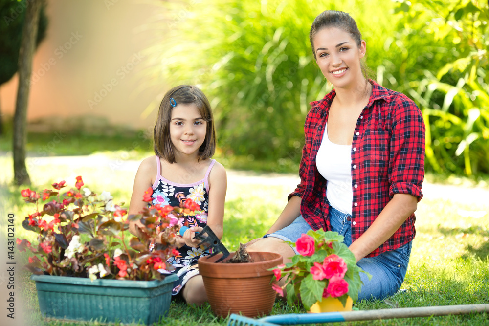 Portrait of beautiful young mother and daughter gardening together in front or back yard