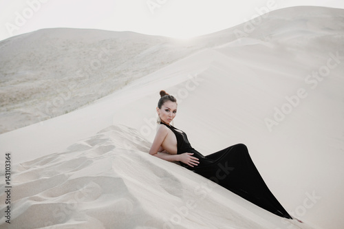 Beautiful sexy asian woman in a black dress on a dune of desert photo