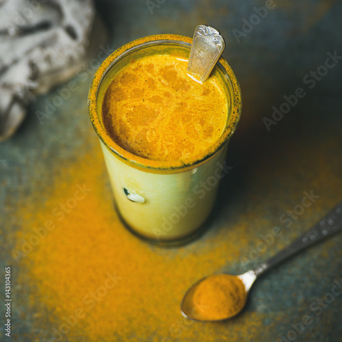 Golden milk with turmeric powder in glass over dark background, copy space, square crop. Health and energy boosting, flu remedy, natural cold fighting drink. Clean eating, weight loss concept