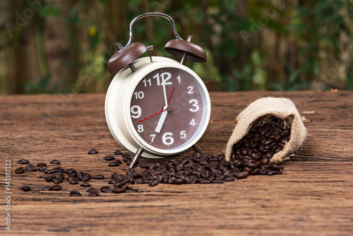 In selective focus of Vintage brouwn clock face and and coffee bean in sack fall on wooden table outdoor background.Coffee break for relax time concept- Vintage effect style pictures. photo