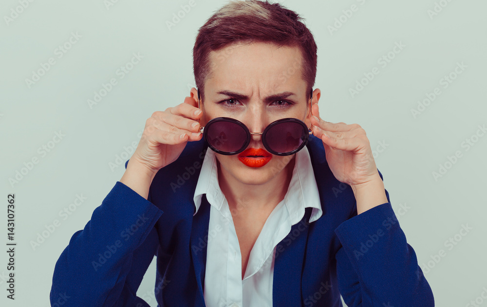 Headshot serious angry bitchy woman wife holding sunglasses down skeptically looking at you isolated green yellow wall background, blue shirt. Human face expression body language, attitude, perception