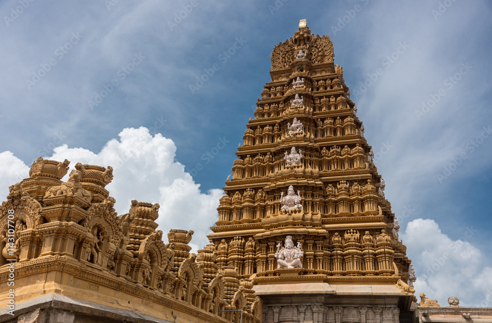 Nanjangud, India - October 26, 2013: Main Gopuram of Sri Srikanteshware temple in Ganjangud, Karnataka State. Part of the decorate Mandapam roof in front. Golden decoration, white statues. Cloudscape.