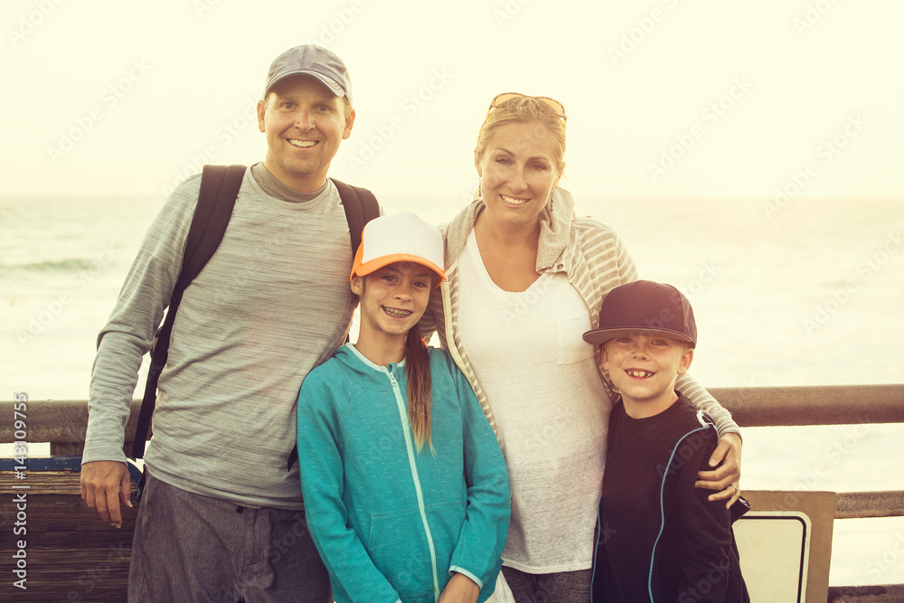 Smiling happy family enjoying their time together during a summer trip to the ocean. Standing together with the sunset behind them as they enjoy their time together Smiling happy family enjoying their time together during a summer trip to the ocean. Standing together with the sunset behind them as they enjoy their time together