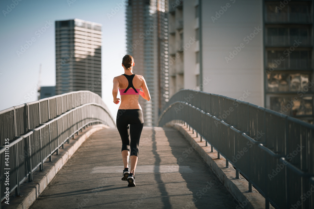 Female runner running on city bridge. 