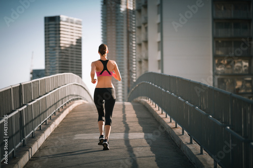 Female runner running on city bridge. 