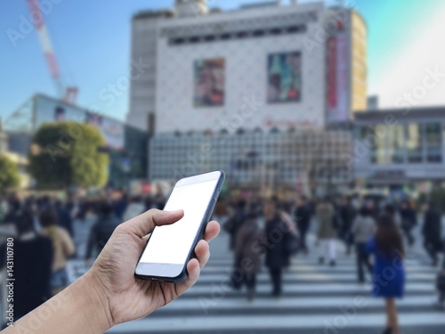 Photography Hand holding mobile smart phone with a crowd of people in Shibuya Crossing