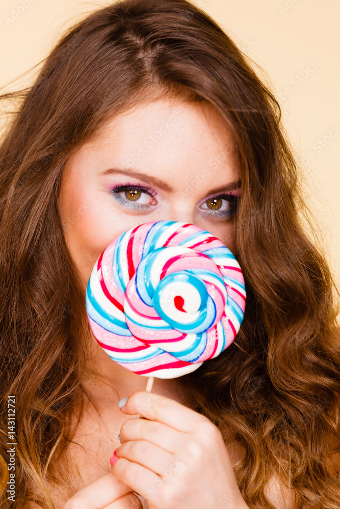 Woman holds colorful lollipop candy in hand, covering face