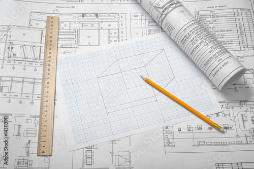 A set of open and rolled up blueprints on wooden table background with a pencil and a ruler lying beside.
