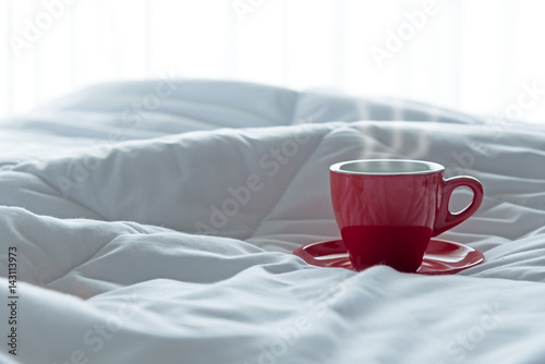 Fresh morning coffee in red cup on the bed.