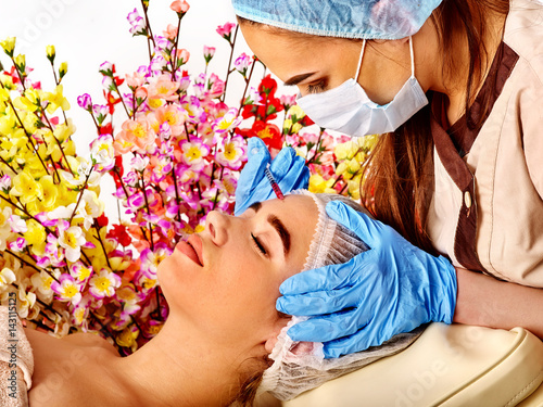 Filler injection for female forehead face. Plastic aesthetic facial surgery in beauty clinic. Woman giving botox injections. Doctor in medical gloves and hat with syringe on spring flowers background. photo