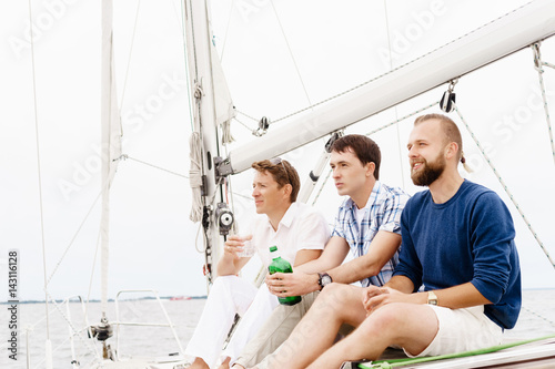 Happy friends sitting together on a deck of a yacht and drinking an alcoholic drink.