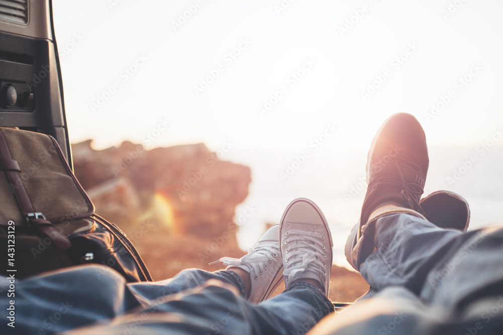 Couple lying at sunset near the ocean in the car's trunk, close-up of shoes of woman and man, romantic relationships - obrazy, fototapety, plakaty 